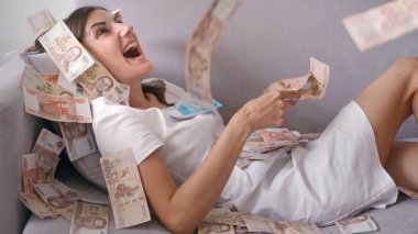 Many banknotes fly in the air overhead in slow motion. A girl lies and a lot of money falls on her. happy woman rejoices huge wealth of money clipart