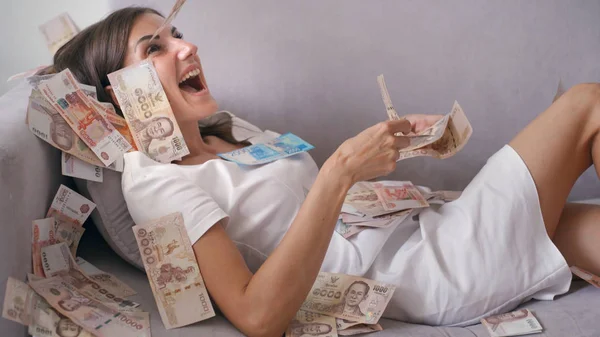 Many banknotes fly in the air overhead in slow motion. A girl lies and a lot of money falls on her. happy woman rejoices huge wealth of money — Stock Photo, Image