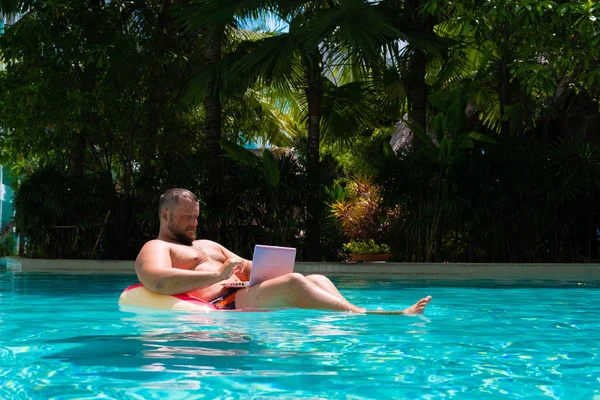Male freelancer with a laptop on rubber ring in the water — Stock Photo, Image