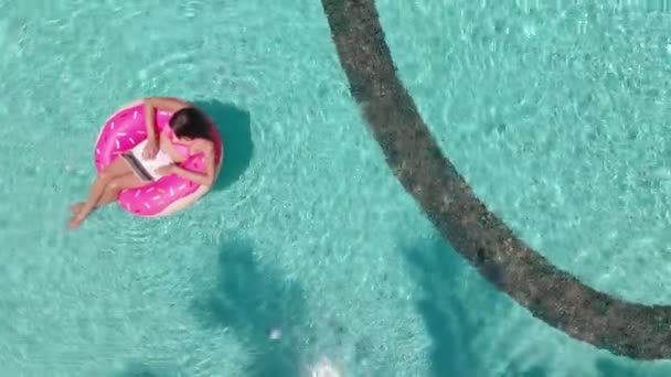 Young female freelancer sitting with a tablet in an inflatable circle in the pool. Aerial view — ストック動画