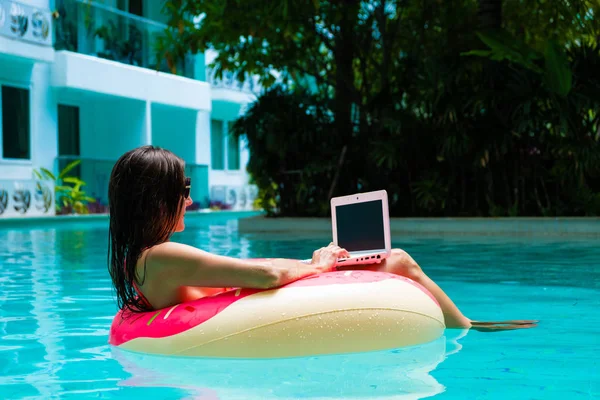 Meisje in de opblaasbare cirkel in het zwembad met een laptop, het concept van Freelancing en recreatie. — Stockfoto