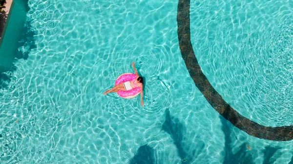 Joven freelancer sentada con una tableta en un círculo inflable en la piscina. Vista aérea —  Fotos de Stock