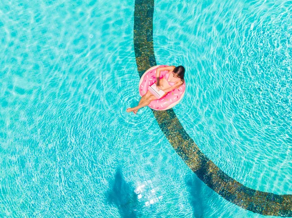 Young female freelancer sitting with a tablet in an inflatable circle in the pool. Aerial view — ストック写真