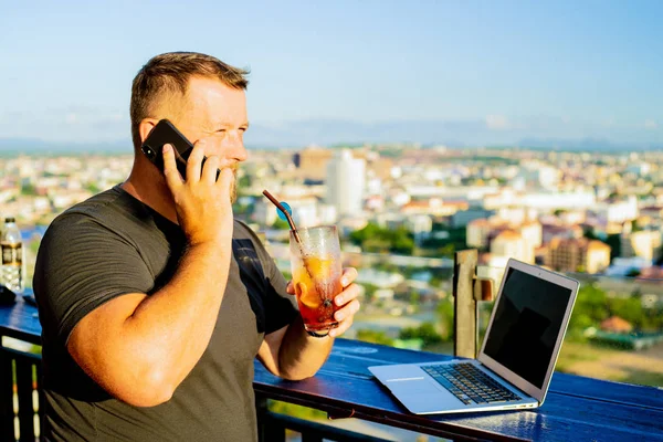 Man praten op de telefoon en werken op een computer in een café met een prachtig uitzicht — Stockfoto