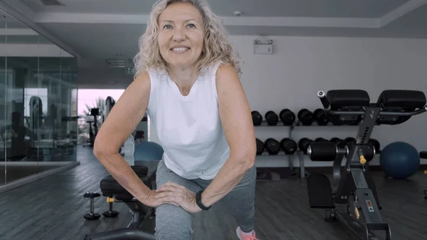 Yaşlı kadın spor salonunda çömelmiş. Yaşlı kadın Yaşlı kadın spor salonunda bir spor egzersizleri yapar
