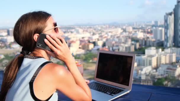 Fêmea falando ao telefone enquanto trabalhava em um computador em um café no telhado com uma vista panorâmica de Pattaya — Vídeo de Stock