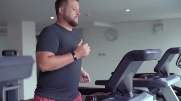 Chubby man walking on running track, warming up on gym treadmill. — Stock Video