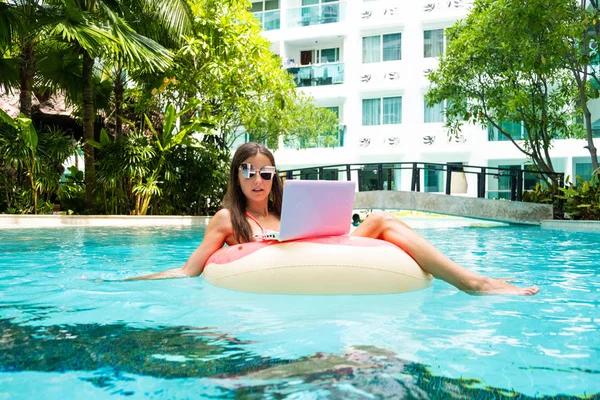 Een jonge vrouw zweeft op zee in een zwem cirkel. Een meisje is ontspannen op de zee op de opblaasbare ring met mini computer. selectieve focus — Stockfoto