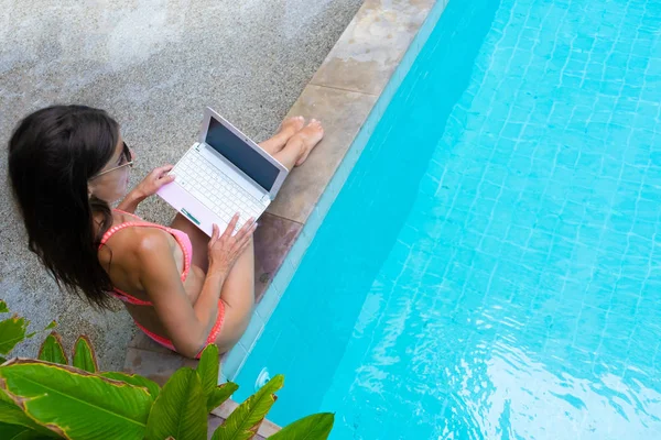Vrouw zit bij het zwembad en daalt de laptop in het water. Het meisje rust op een mini computer. selectieve focus — Stockfoto