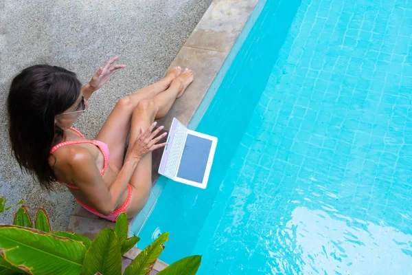 Vrouw zit bij het zwembad en daalt de laptop in het water. Het meisje rust op een mini computer. selectieve focus — Stockfoto