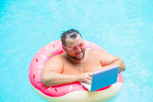 havuzda şişme bir daire üzerinde pembe gözlük komik şişman erkek zevk bir kız tasvir bir dizüstü bilgisayar üzerinde çalışır.