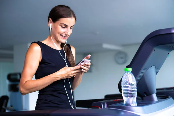 Mujer en forma joven corriendo en la cinta de correr escuchando música a través de auriculares en el gimnasio — Foto de Stock