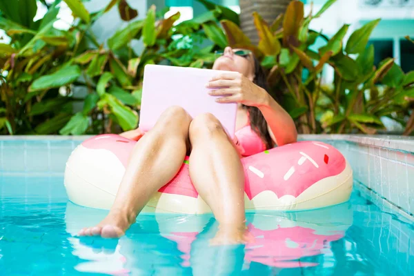 Een jonge vrouw zweeft op zee in een zwem cirkel. Een meisje is ontspannen op de zee op de opblaasbare ring met mini computer. selectieve focus — Stockfoto