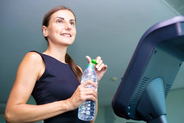 Hermosa chica de fitness corriendo y beber agua en la cinta de correr en el gimnasio — Foto de Stock