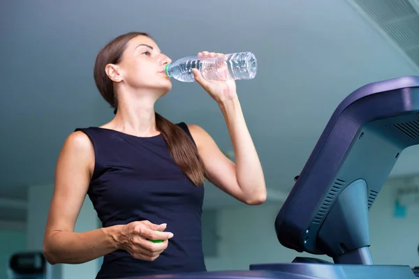 Hermosa chica de fitness corriendo y beber agua en la cinta de correr en el gimnasio — Foto de Stock