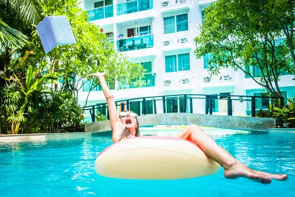 女性はプールのスイミングプールで泳ぎ、ラップトップを水に投げます。少女はミニコンピュータで膨脹可能なリングで海で休んでいる。選択的フォーカス — ストック写真