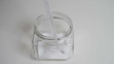 Yavaş yavaş beyaz bir masa ahşap masa üzerinde duran cam kavanoza tuz dökme