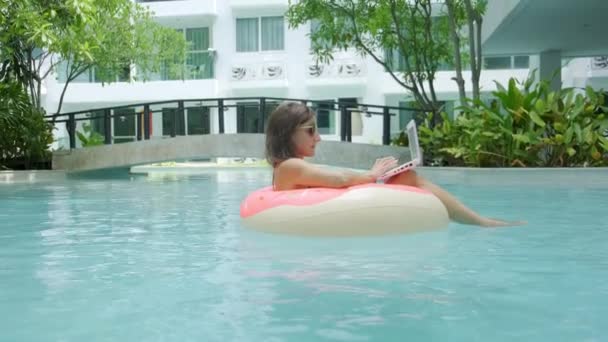 Kobieta płodzi w basenie w basenie i wyrzuca laptopa do wody. Dziewczynka odpoczywa na morzu na nadmuchiwanym pierścieniu z minicomputer. Selektywna koncentracja — Wideo stockowe