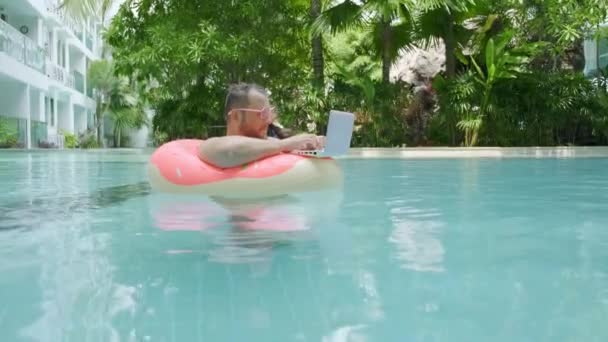 Tłuszcz zabawny człowiek w różowy nadmuchiwane koło zaskoczony i spada laptop do wody w basenie. — Wideo stockowe