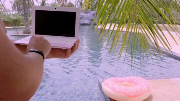 A man is typing on his laptop while sitting by the pool. Mens hands on the keyboard in the pool — Stock Video