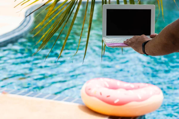 Een man is het typen op zijn laptop terwijl zittend bij het zwembad. Mens handen op het toetsenbord in het zwembad — Stockfoto