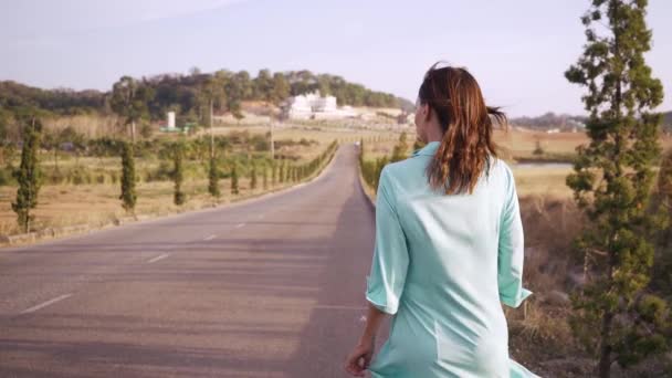 Uma jovem em um vestido verde está andando ao longo de uma estrada direta . — Vídeo de Stock