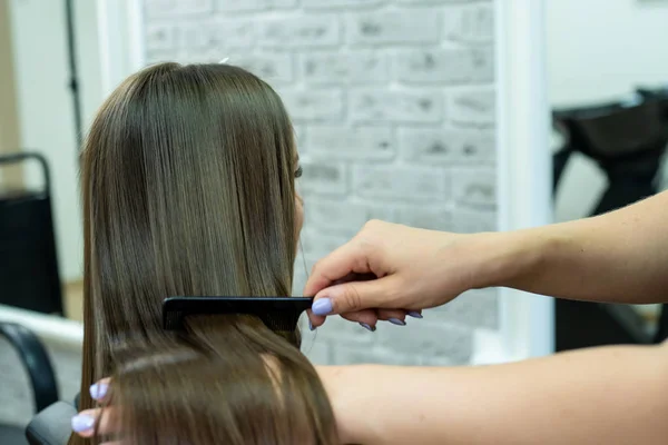 Kuaför esmer saçlı bir kız için bir güzellik salonunda saç laminasyon yapar