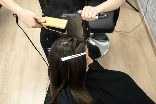 Peluquería hace laminación de cabello en un salón de belleza para una chica con pelo morena —  Fotos de Stock