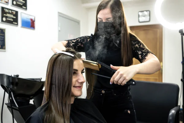 hairdresser makes hair lamination in a beauty salon for a girl with brunette hair