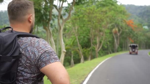 Bonita floresta tropical com um jovem viajante com uma mochila na estrada para a floresta da Tailândia. Um homem caminha em uma estrada tropical e desfruta das vistas da natureza — Vídeo de Stock