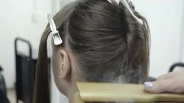 Kuaför esmer saçlı bir kız için bir güzellik salonunda saç laminasyon yapar
