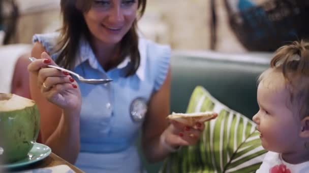 Το πορτρέτο μιας μητέρας που κάθεται με το κοριτσάκι της στο εστιατόριο και μοιράζεται ένα γεύμα. Η έννοια της πρώτης σίτισης για τα παιδιά. — Αρχείο Βίντεο
