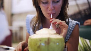 Mavi elbiseli güzel kadın akşam bir kafede bir saman hindistan cevizi içecekler, yakın çekim.