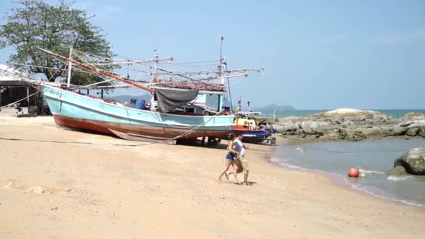 愛の男女のカップルは、タイの伝統的なボートを背景に晴れた日に海にジャンプするために遊歩道の端に実行します — ストック動画