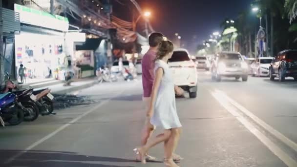 Relaciones románticas y amorosas. pareja joven macho y hembra cruzan la calle por la noche en Pattaya, Tailandia, vista trasera . — Vídeos de Stock