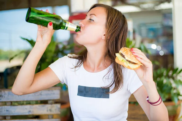 Genç çekici kız, bağımsız bir görünüm ile, bira içecekler ve bir burger yiyor. Yakından kapatın. Feminizm ve kadınların bağımsızlığı kavramı. — Stok fotoğraf