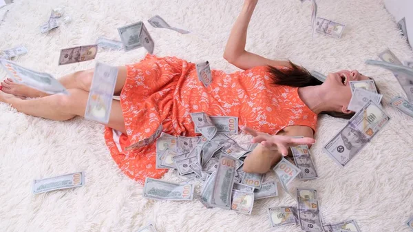 A lot of money, a view from the top, a girl in a cropped dress collects them. Throws, rejoices. Lies in the money they fall on her from the top. — Stock Photo, Image