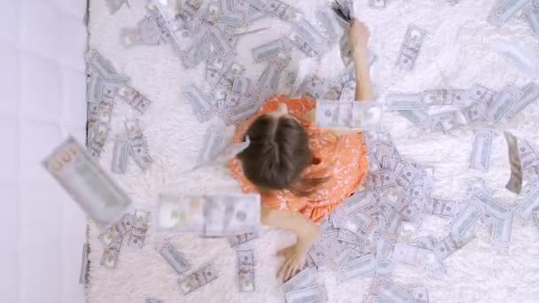 Spousta peněz, výhled shora, je sbírá dívka v ořezávanýma šatech. Hází, raduje. Leží v penězích, které na ní padají shora. — Stock video