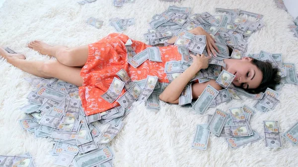 A lot of money, a view from the top, a girl in a cropped dress collects them. Throws, rejoices. Lies in the money they fall on her from the top. — Stock Photo, Image