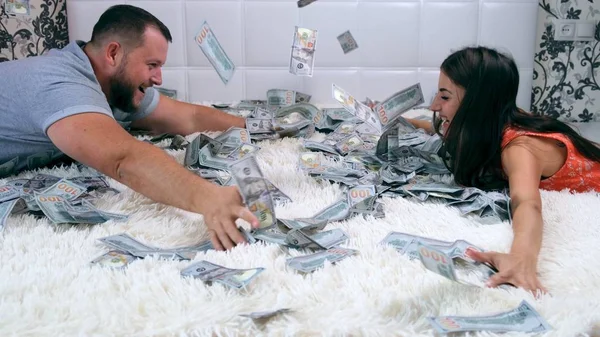A man and woman share money sitting on a white bed, have fun rushing denbgs and consider them. View from above. Lot of money.Fast money concept — Stock Photo, Image