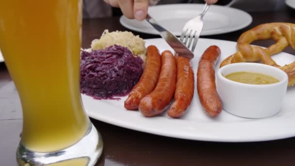 Тарілка з німецькими ковбасами і капуста поруч зі склянкою пива, клієнт ставить його тарілку. Зачиніть. — стокове відео