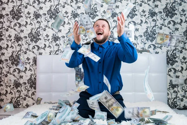 A nice man with a beard in a blue shirt, rejoices at the dollars, throws them up and counts. Win lottery — Stock Photo, Image