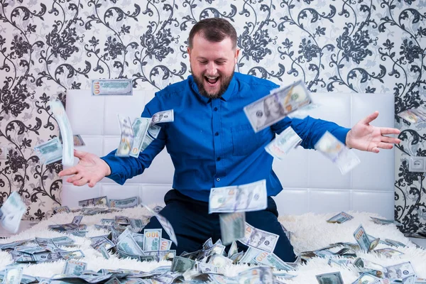 A nice man with a beard in a blue shirt, rejoices at the dollars, throws them up and counts. Win lottery — Stock Photo, Image