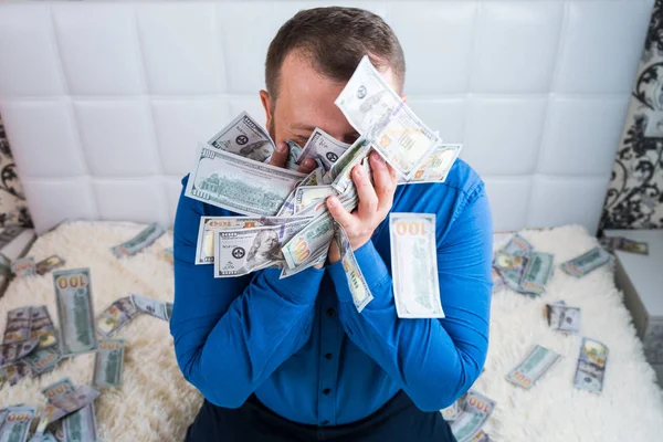 A nice man with a beard in a blue shirt, rejoices at the dollars, throws them up and counts. Win lottery — Stock Photo, Image