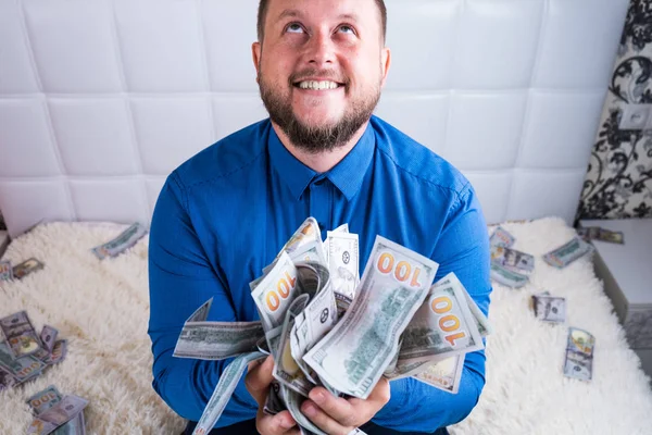 A nice man with a beard in a blue shirt, rejoices at the dollars, throws them up and counts. Win lottery — Stock Photo, Image