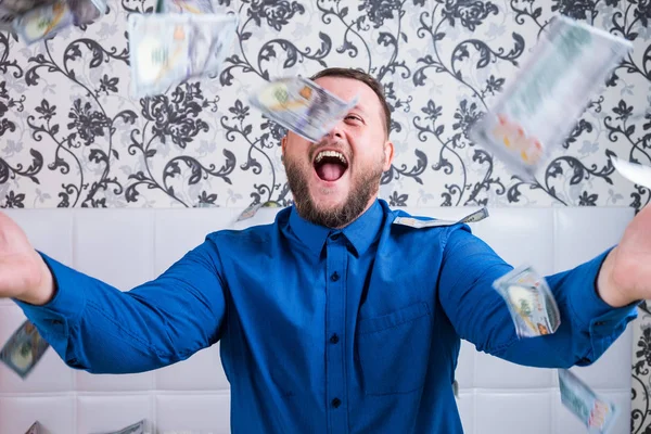 A nice man with a beard in a blue shirt, rejoices at the dollars, throws them up and counts. Win lottery — Stock Photo, Image