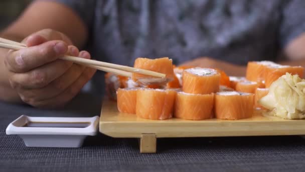 Homem gordinho agradável com barba num bar de sushi, a comer pãezinhos. Não sabe como lidar com paus, rolos caem . — Vídeo de Stock