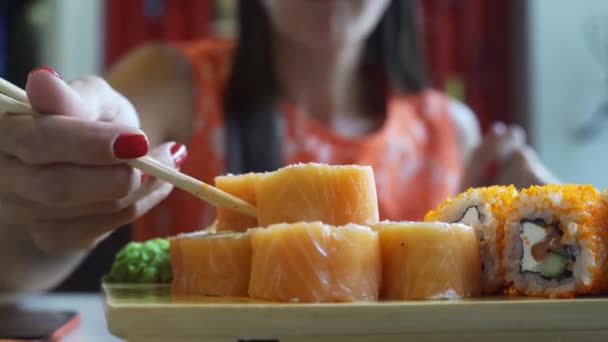 Mujer agradable en un bar de sushi, comiendo rollos con el dedo palo. De cerca. — Vídeo de stock