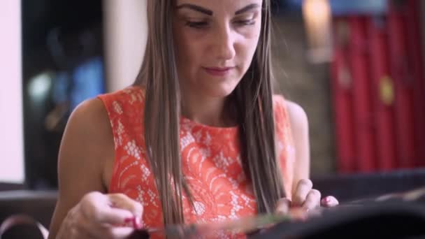 En kvinna på ett kafé, dricker en smoothie, Leafs genom menyn, läser meddelanden på telefonen och skriver svaret. Närbild — Stockvideo