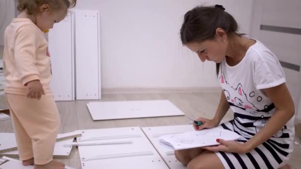 A young woman with her daughter, assemble furniture according to the instructions, hammering nails with a hammer, tighten the screws with a screwdriver. — Stock Video